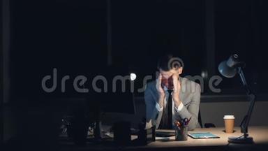 一个穿着西装的疲惫的年轻人正在电脑上工作，深夜独自坐在办公室完成工作，擦着脸
